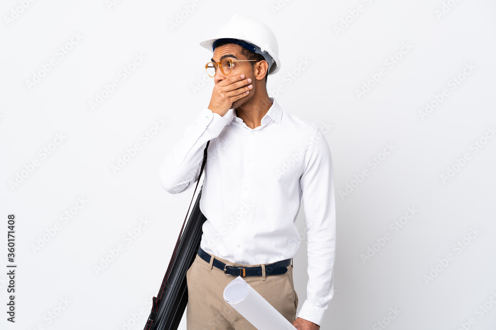 African American architect man with helmet and holding blueprints over isolated white background _ covering mouth and looking to the side African American architect man with helmet and holding blueprints over isolated white background _ covering mouth and looking to the side