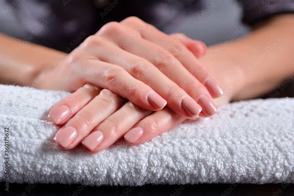 Female hands with nude color nails polish on a towel in beauty studio. Girl holding hand on desk and nails colored with natural nude shade color. Manicure concept. Close up, selective focus