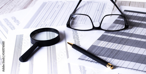 On the reports is a pen, a magnifying glass, glasses in black frames. Business concept