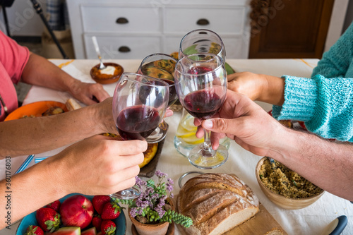 Four people friends or family toasting with red wine glasses having fun together around the table with vegetarian food. Healthy eating and relax concept