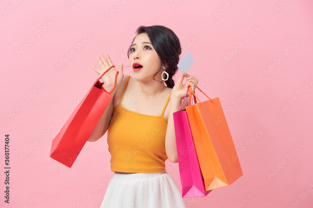 Portrait of a beautiful girl wearing dress and holding colorful shopping bags and showing credit card isolated over pink background Portrait of a beautiful girl wearing dress and holding colorful shopping bags and showing credit card isolated over pink background