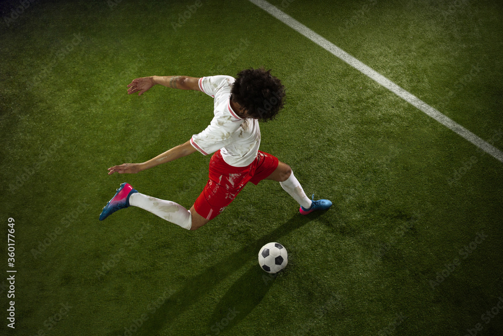 Obraz premium Top view of caucasian football or soccer player on green background of grass. Young male sportive model training in action. Kicking ball, attacking, catching. Concept of sport, competition, winning.