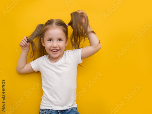 A naughty little girl in a white T-shirt is holding herself by the hair on a yellow background. Mocap. Copyspace