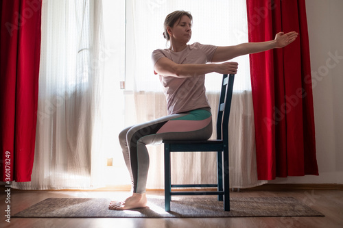 Woman working out doing yoga or pilates exercise using chair. Ardha Matsyendrasana pose variation. photo