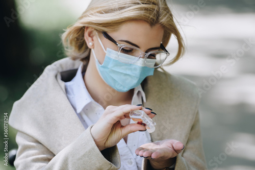 woman wearing medical mask using hand sanitizer 