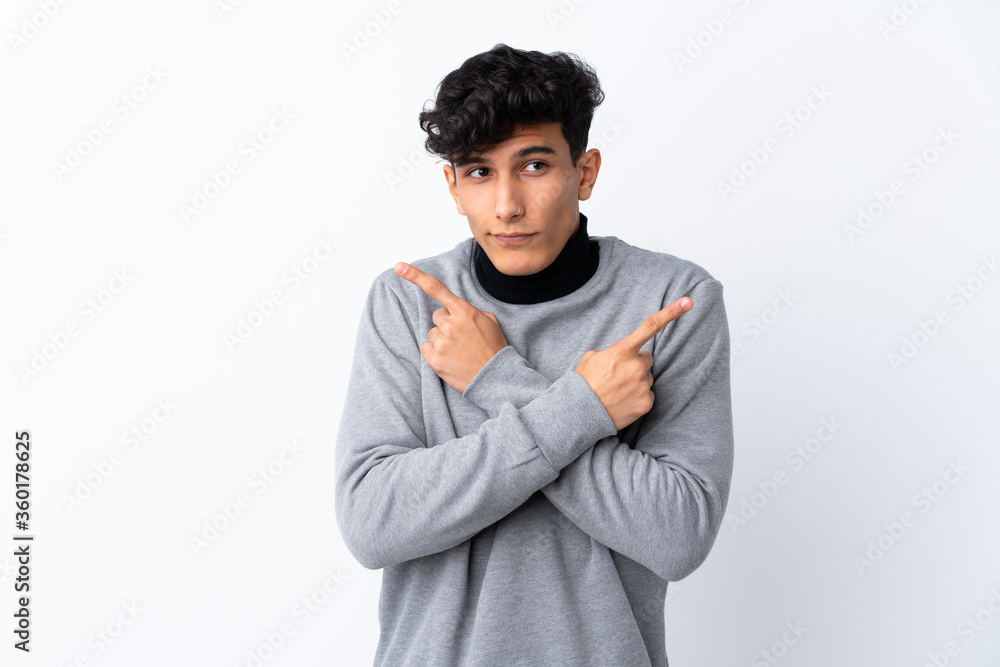 Young Argentinian man over isolated white background pointing to the laterals having doubts Young Argentinian man over isolated white background pointing to the laterals having doubts