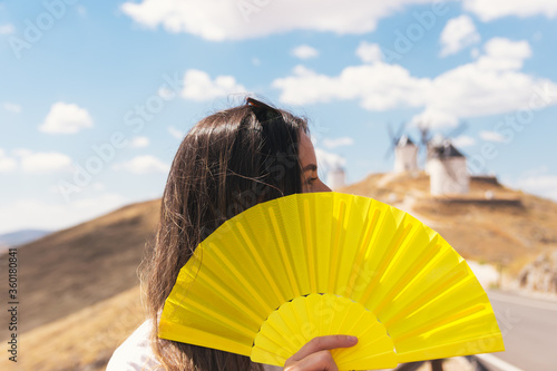 Blonde girl with a yellow fan in her hands. Traditional windmills of Consuegra in the background.