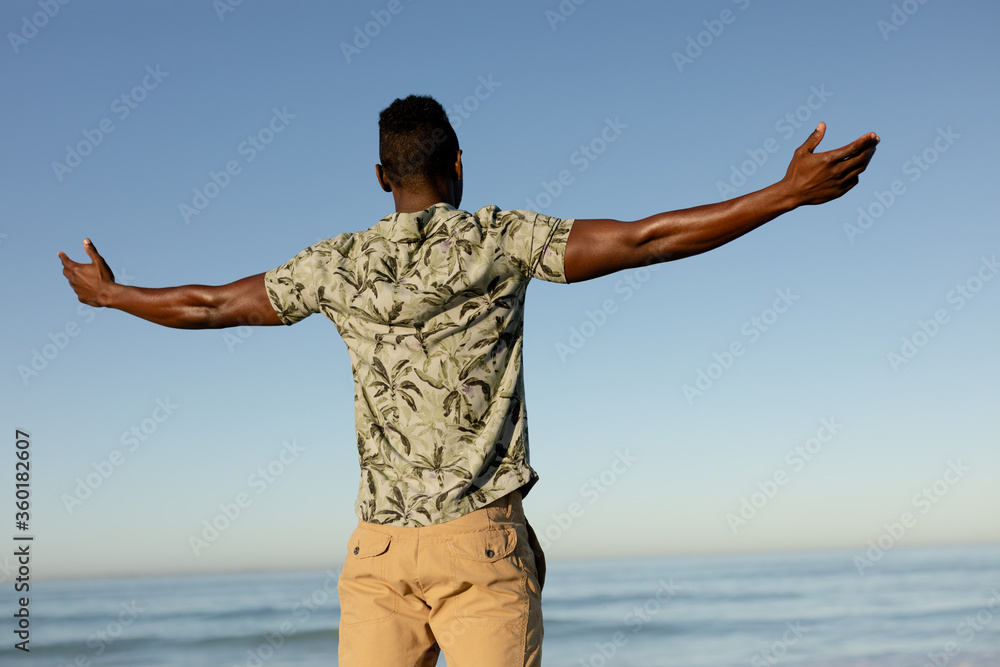 An African American man with his arms outstretched on beach on a sunny day