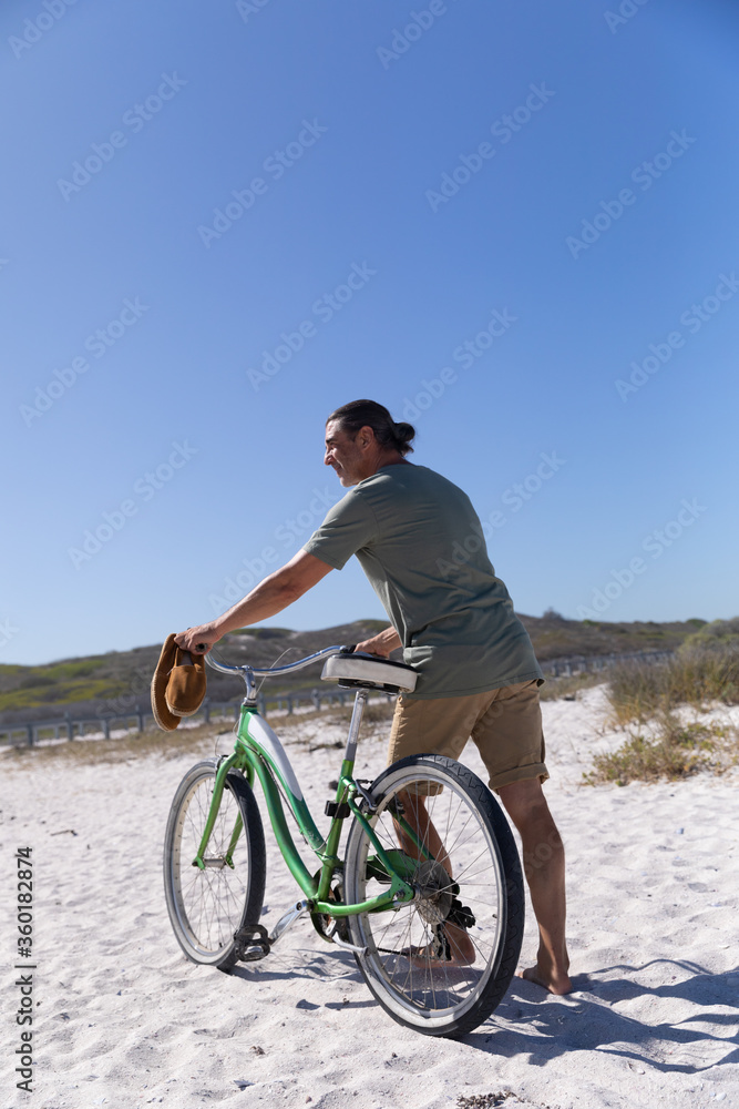 Fototapeta premium Senior Caucasian man carrying a bike at the beach 