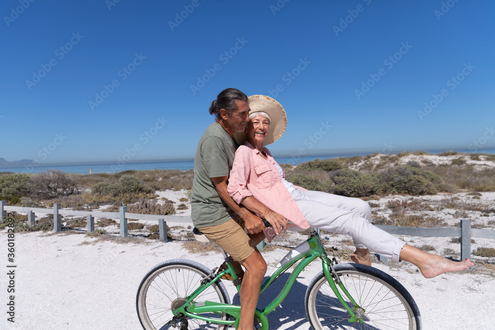 Fototapeta premium Senior Caucasian couple riding a bike at the beach
