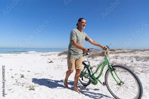 Senior Caucasian man carrying a bike at the beach 
