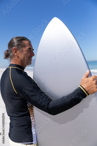 Senior Caucasian man holding a surfboard at the beach.