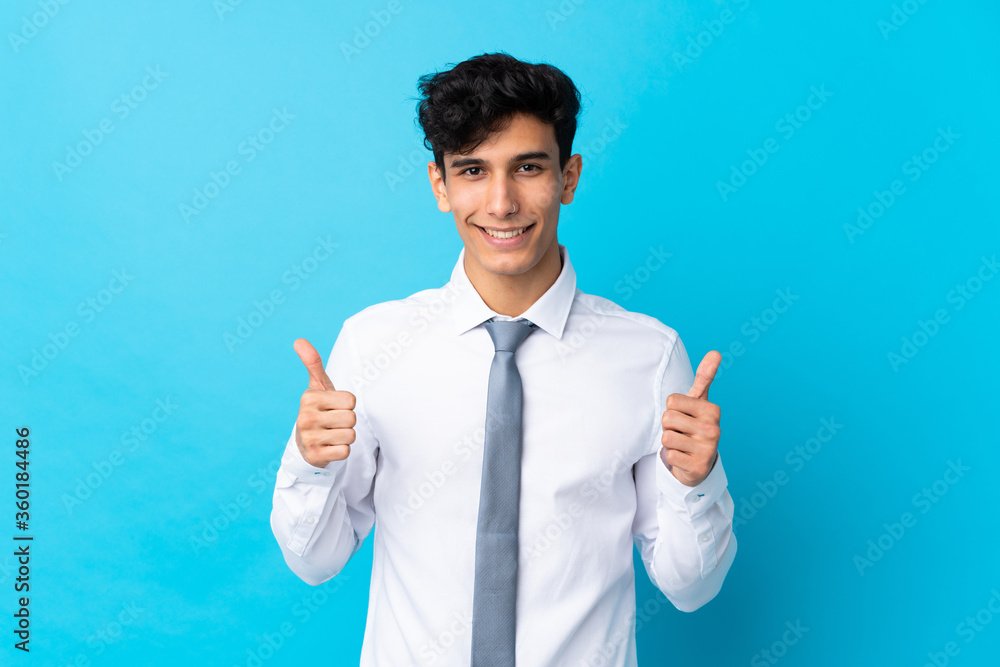 Young Argentinian businessman over isolated blue background giving a thumbs up gesture
