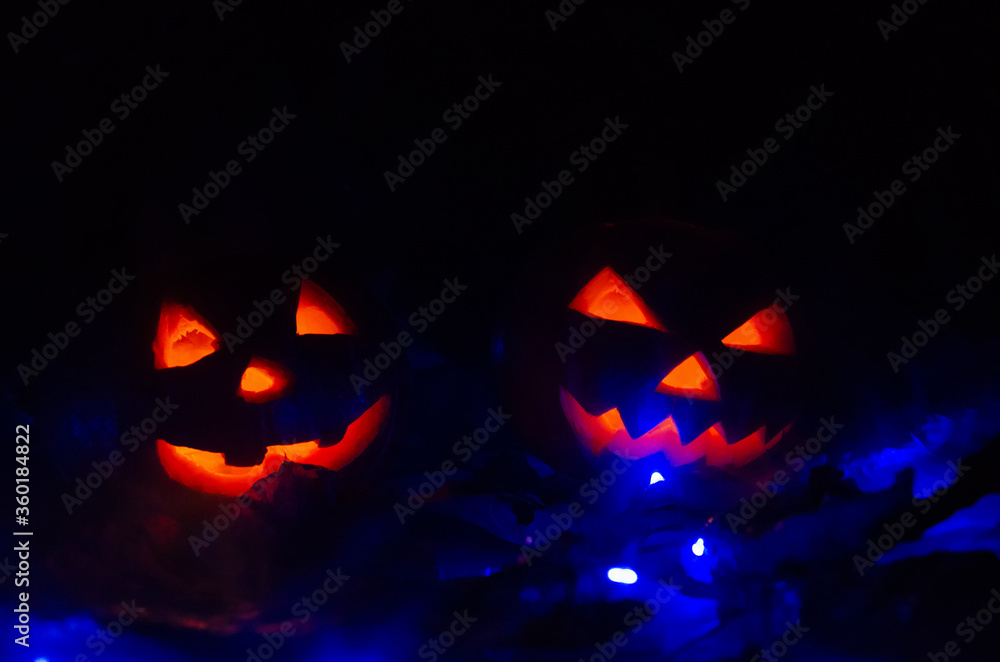 Scary two glowing pumpkins in the dark with a blue backlight close-up. concept of the Halloween background. Scary two glowing pumpkins in the dark with a blue backlight close-up. concept of the Halloween background.