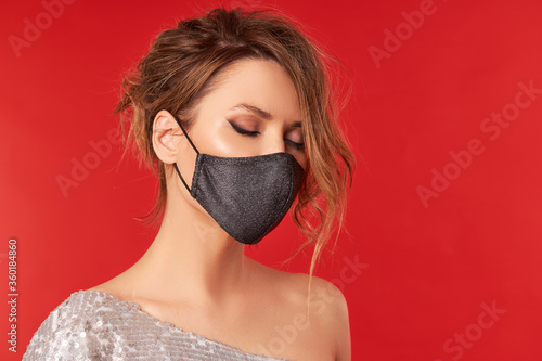 Upset woman in trendy fashionable outfit during quarantine. Model dressed stylish protective face mask on red studio background