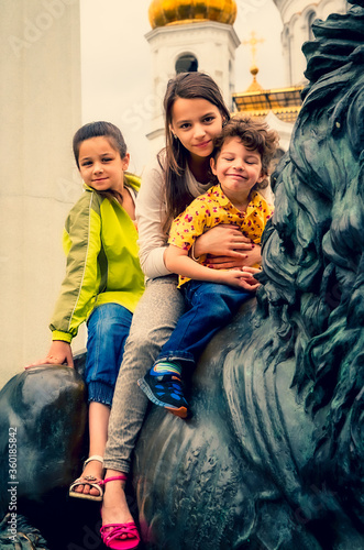 A family of three children sitting on a stone animal in the historical center of Moscow