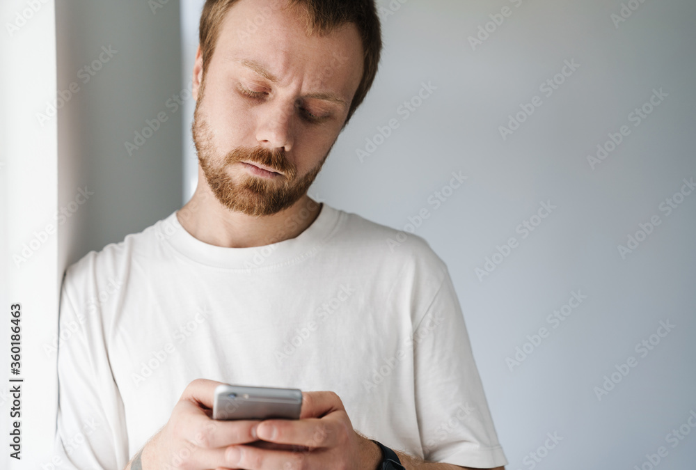 Photo of perplexed bearded man with red hair using mobile phone Photo of perplexed bearded man with red hair using mobile phone