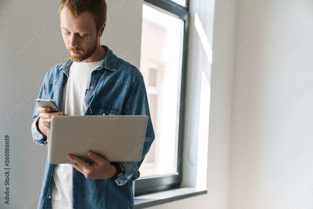 Photo of focused man typing on cellphone and working with laptop Photo of focused man typing on cellphone and working with laptop