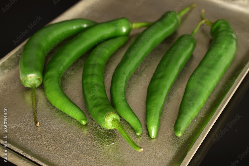 Green chili peppers on a metal tray, on a black background. Green chili peppers on a metal tray, on a black background.