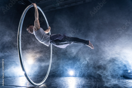 Cyr Wheel circus artist on smoked, dark background performing on stage  photo