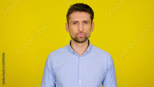 Confident bearded man in a blue shirt on yellow background with a place for text looks at the camera