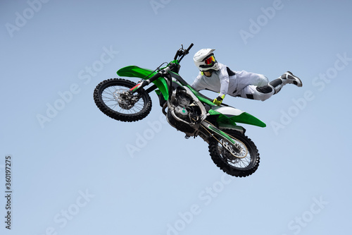Ricer in a white protective uniform and helmet shares a stunt in the air on a motorcycle. jump and flight on a motorcycle. extreme sport. motor freestyle