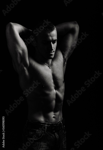 Athletic man's torso. Unrecognizable male fitness model show naked muscular body. Strong muscles and biceps. Studio shot on black background, monochrome, black and white. Bodybuilding concept