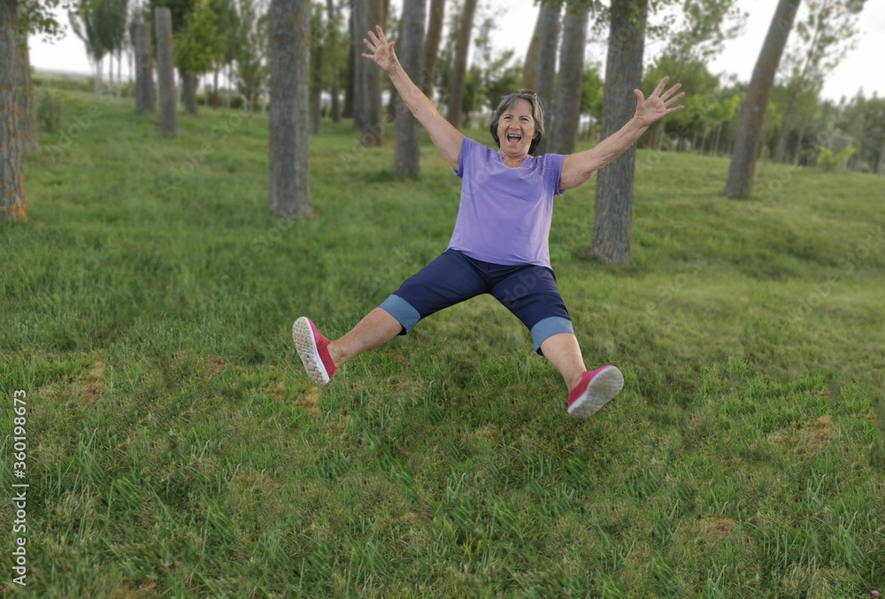Naklejka premium Older lady, older woman, grandmother, jumping for joy on the lawn. positivism and energy