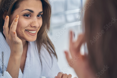 Charming young woman looking in the mirror in bathroom