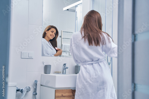 Cheerful young woman brushing hair in bathroom