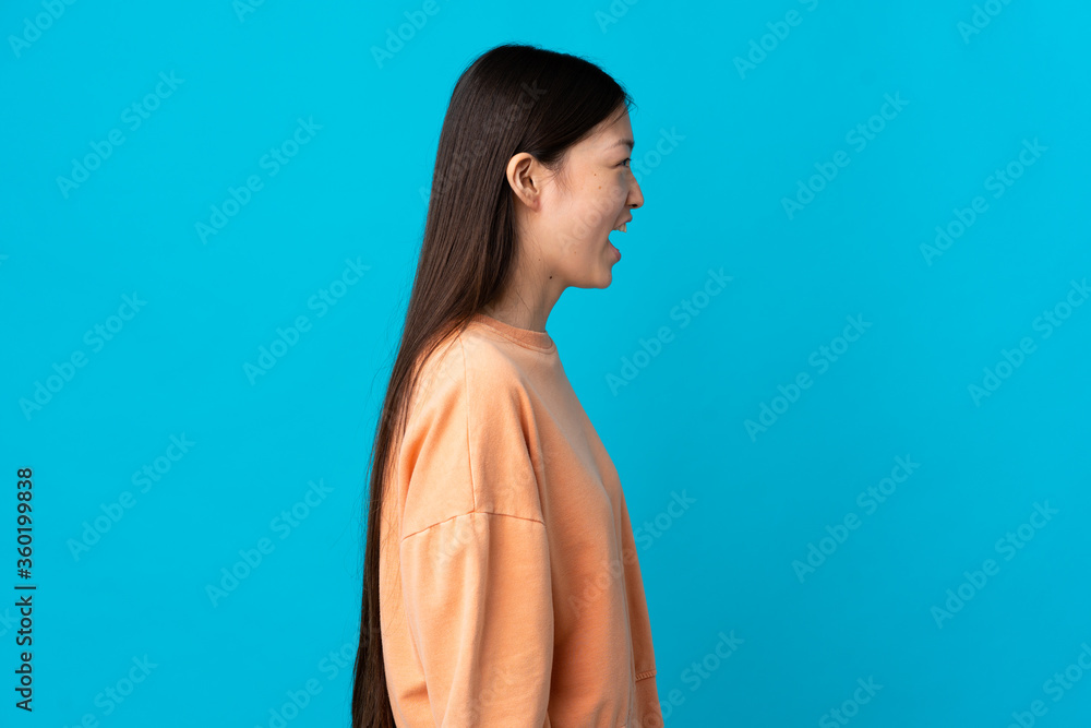 Young Chinese girl over isolated blue background laughing in lateral position Young Chinese girl over isolated blue background laughing in lateral position