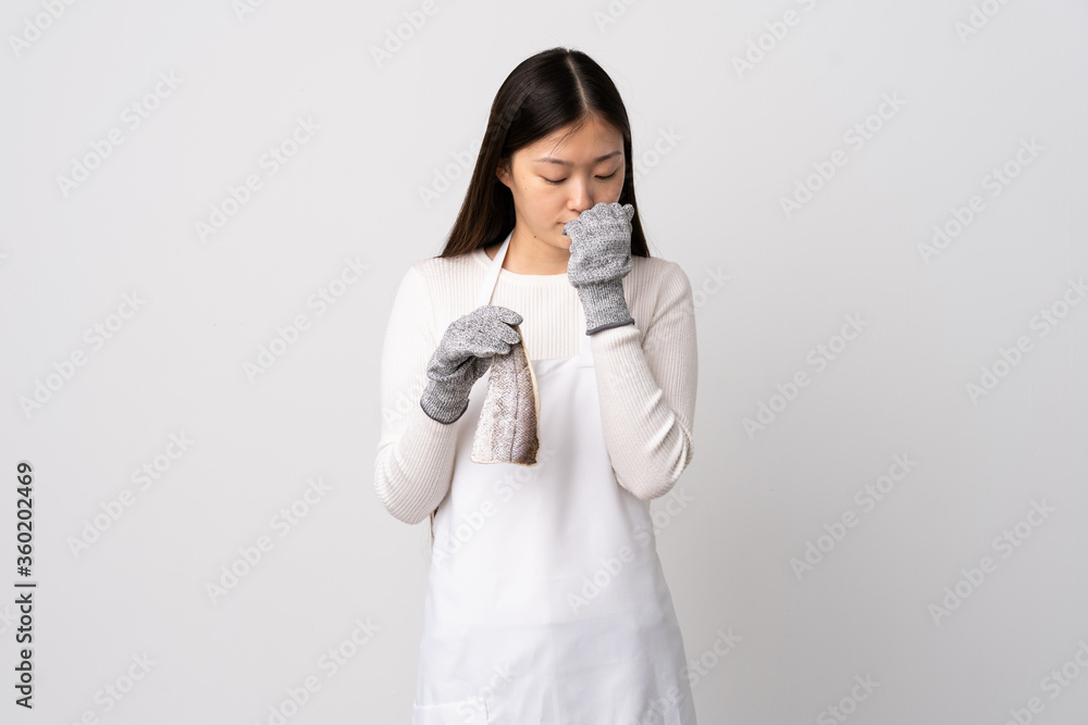 Chinese fishmonger wearing an apron and holding a raw fish over isolated white background having doubts