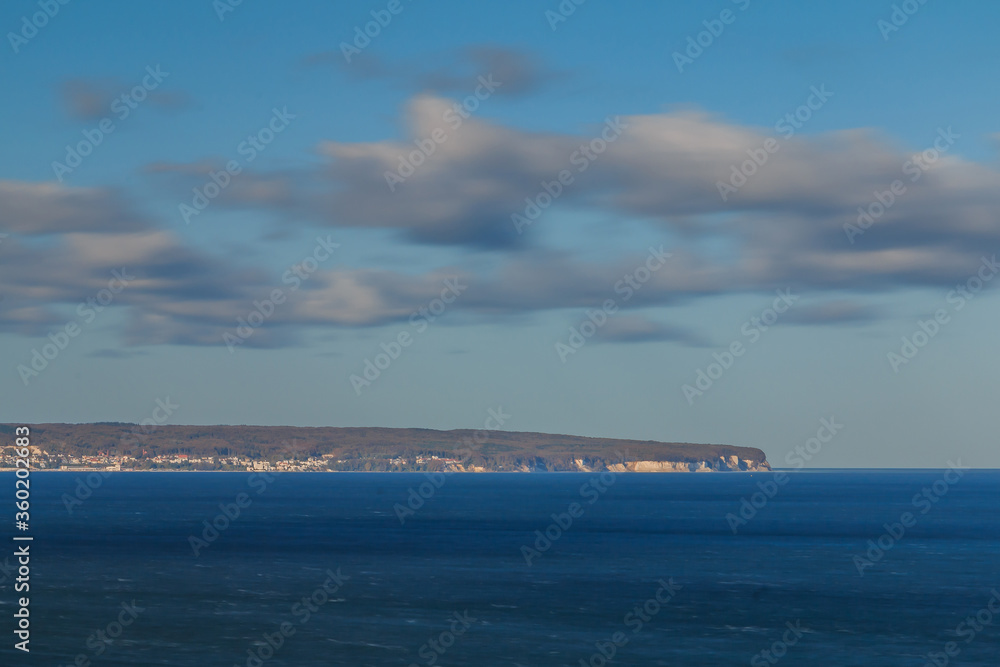 View from the cliffs of the chalk cliff on the island of Ruegen in the Jasmund National Park. Baltic Sea during the day with peninsula on the horizon. Clouds and blue sky with calm sea