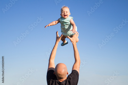 Dad throws his child up against the blue sky. Concept game with children, happy family