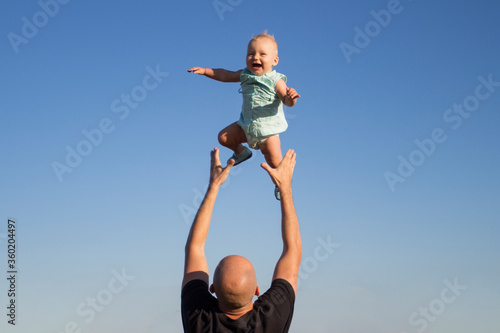 Dad throws his child up against the blue sky. Concept game with children, happy family