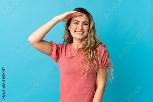 Young Brazilian woman isolated on blue background saluting with hand with happy expression