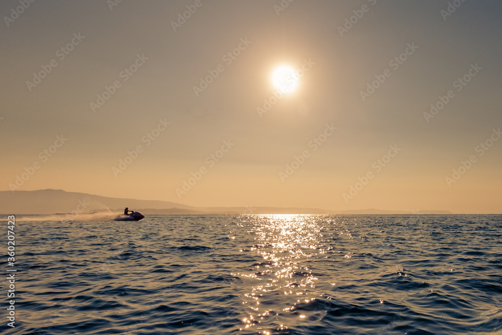 man rides a jet ski in the sea at sunset