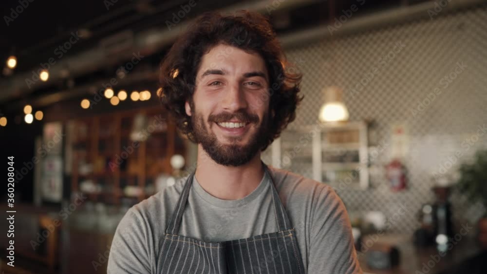 Portrait of cheerful cafe owner wearing black apron standing with folded arms against counter Portrait of cheerful cafe owner wearing black apron standing with folded arms against counter