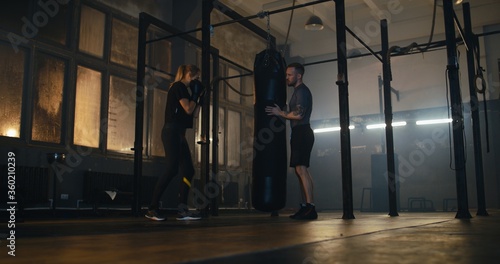 Female boxer hitting a huge punching bag at a boxing studio. Woman boxer practicing with boxing trainer
