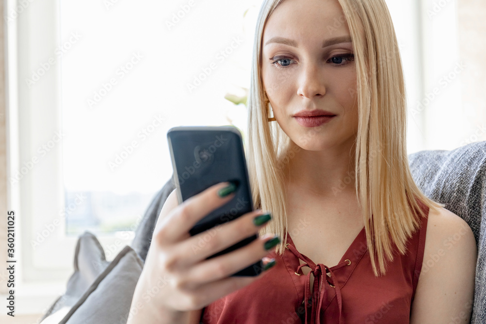 Close-up portrait of a blonde girl with a smartphone indoors Close-up portrait of a blonde girl with a smartphone indoors