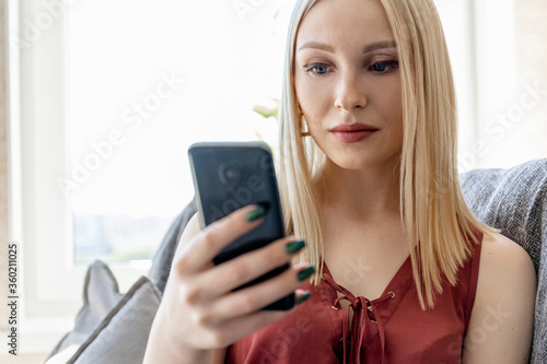 Close-up portrait of a blonde girl with a smartphone indoors