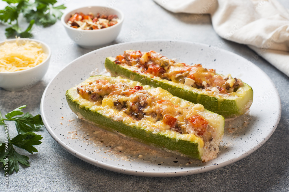 Baked stuffed zucchini boats with minced chicken mushrooms and vegetables with cheese on a plate.