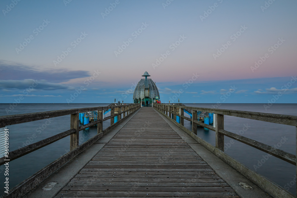 Wooden walkway with railings along the coastline and diving bell at the end. Pier on the Baltic Sea in the evening. Evening horizon with clouds and calm sea on the island of Ruegen
