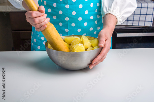 Cooking potato pie fillings (quiche, dumplings). Female hands hold a wooden potato masher in the home kitchen. Close up, selective focus, backlight photo