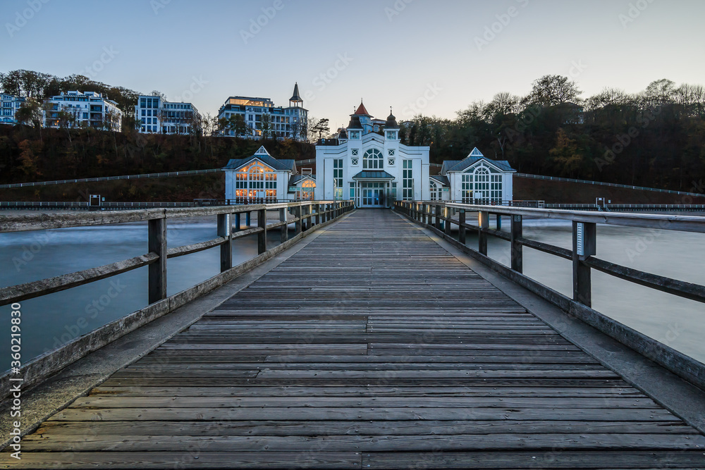 Wooden pier in the evening with a view of Sellin. Coastal section with a jetty without lighting and the buildings on the coastline. Baltic Sea in autumn at the lido with waves