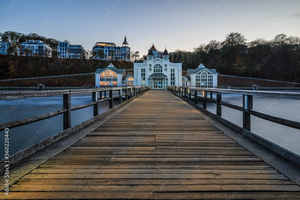 Pier on the Baltic Sea. Illuminated wooden walkway on the island of Ruegen with a historic building in the evening for the autumn mood. Clear blue horizon over buildings in the background
