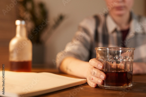 Close-up of young woman sitting at the table and drinking alcohol cocktail at home