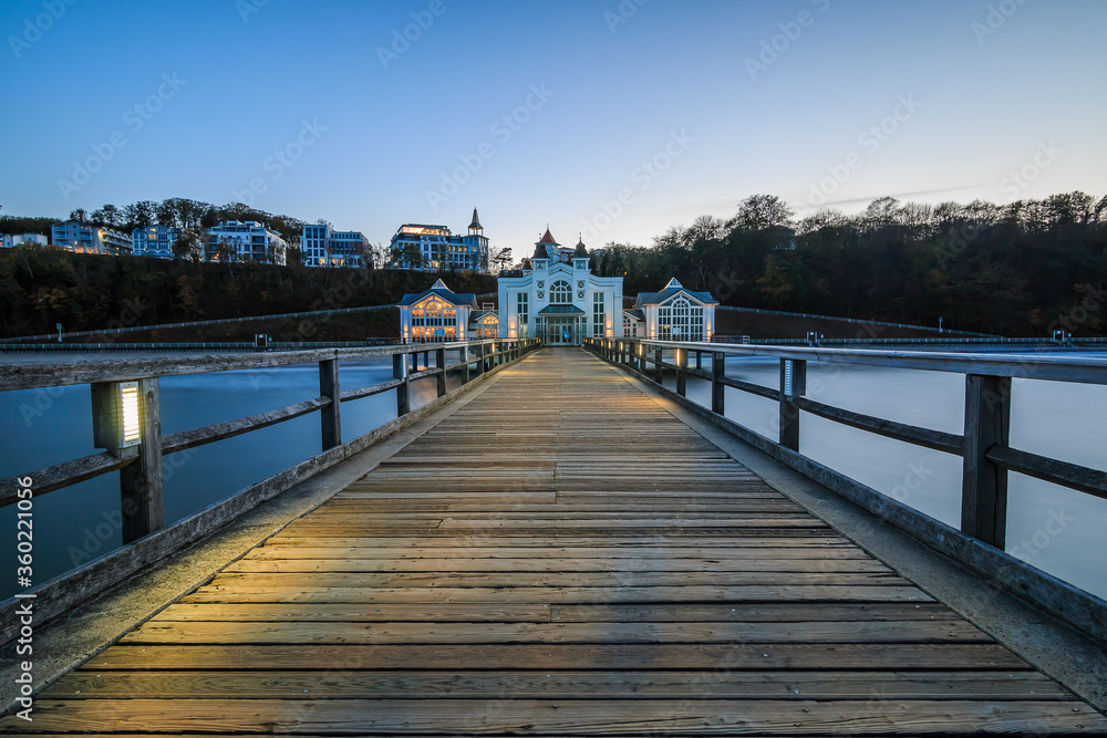 Pier on the Baltic Sea on the island of Ruegen. Illuminated wooden walkway with historical building in the evening for the autumn mood. Clear blue horizon over buildings in the background