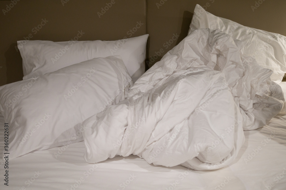 untidy and messy hotel room or home bedroom with pillow, blanket, and mattress sheet spread around unmade for cleaning or maid service concept