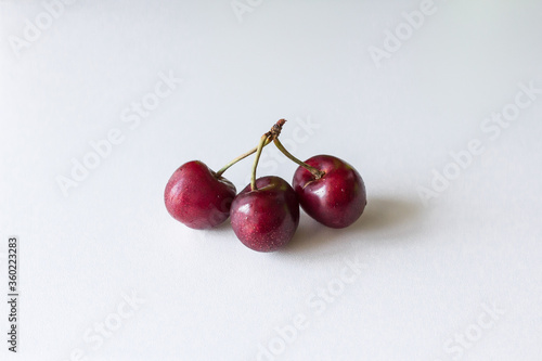 Several berries on one stalk. Metaphor of treason. Third wheel. Two or three cherries. Vitamins in red fruits. Products on a white background. Healthy summer fruits and berries.